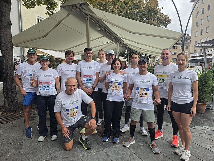 Das Laufteam der Winzer Krems beim Wachaumarathon 2026. Es ist ein Gruppenfot mit insgesamt 11 Personen, die alle ein weißes WINZER KREMS-Laufshirt tragen. 
